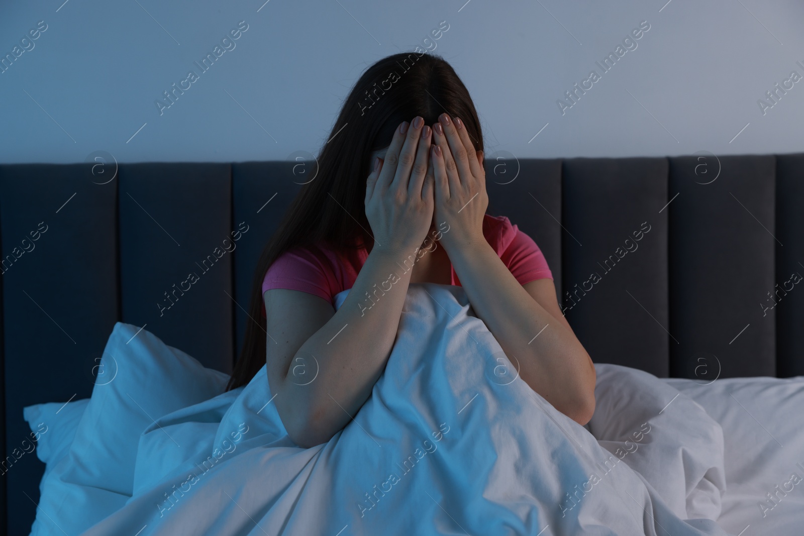 Photo of Fear of darkness. Scared young woman on bed and hiding her face in room at night