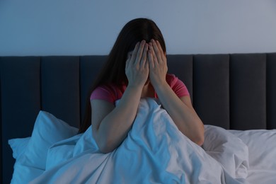 Photo of Fear of darkness. Scared young woman on bed and hiding her face in room at night