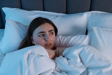 Photo of Fear of darkness. Scared young woman lying on bed in room at night, space for text