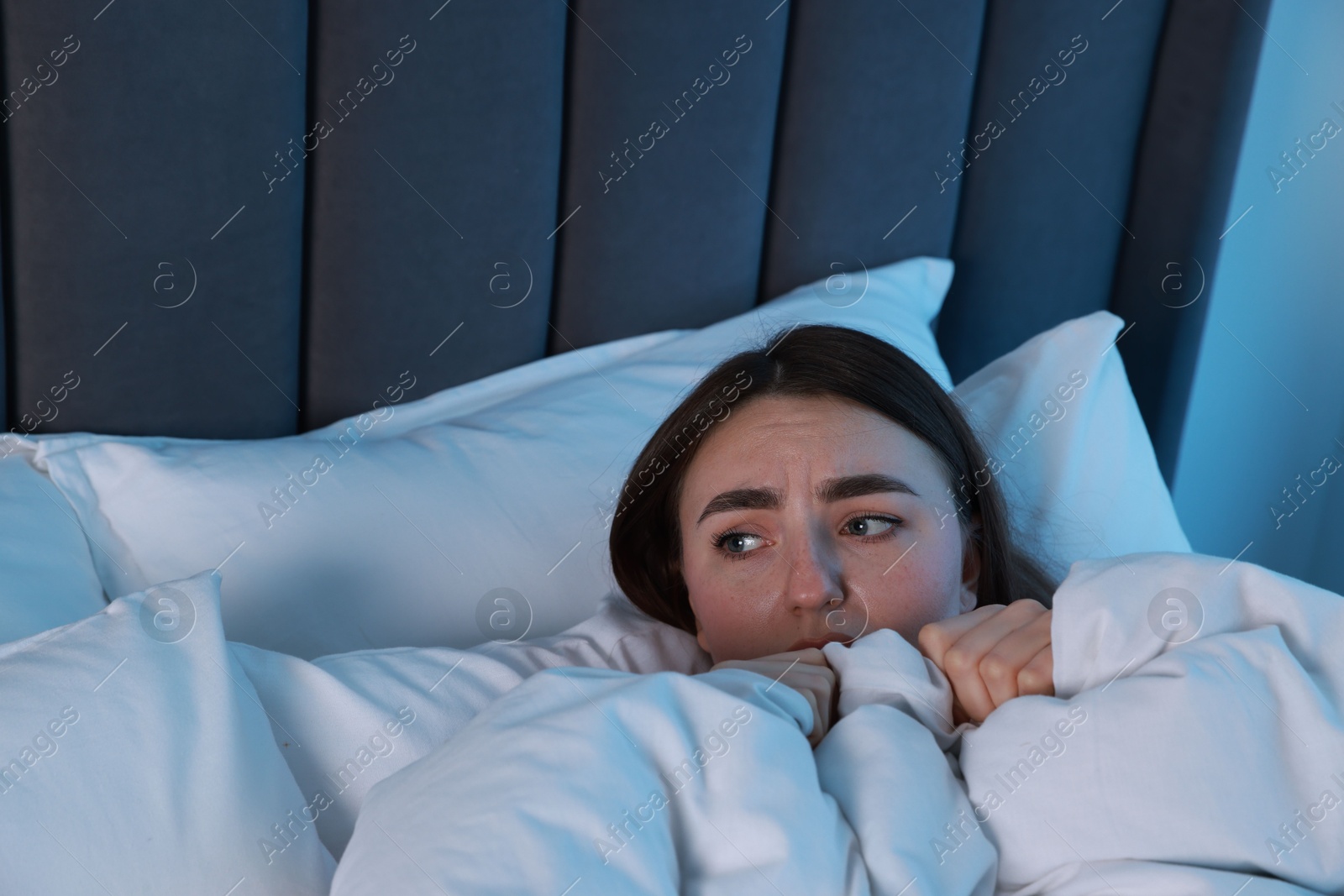 Photo of Fear of darkness. Scared young woman lying on bed in room at night