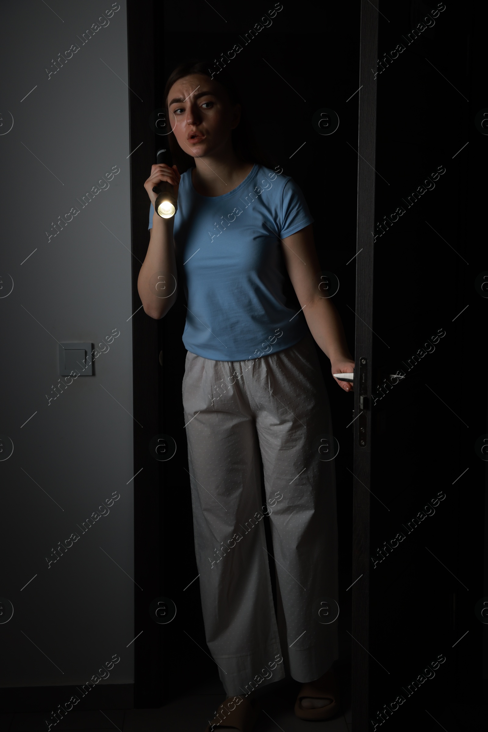 Photo of Fear of darkness. Scared young woman with flashlight indoors at night