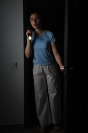 Fear of darkness. Scared young woman with flashlight indoors at night