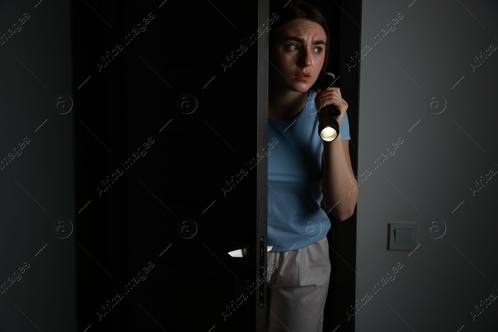 Photo of Fear of darkness. Scared young woman with flashlight indoors at night, space for text