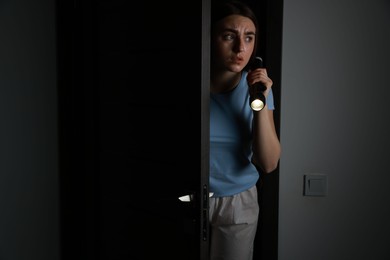 Fear of darkness. Scared young woman with flashlight indoors at night, space for text