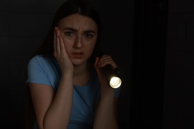 Photo of Fear of darkness. Scared young woman with flashlight indoors at night, space for text