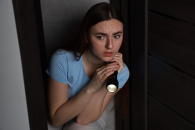 Photo of Fear of darkness. Scared young woman with flashlight indoors at night