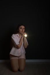 Fear of darkness. Scared young woman with flashlight indoors at night