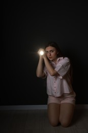 Fear of darkness. Scared young woman with flashlight indoors at night