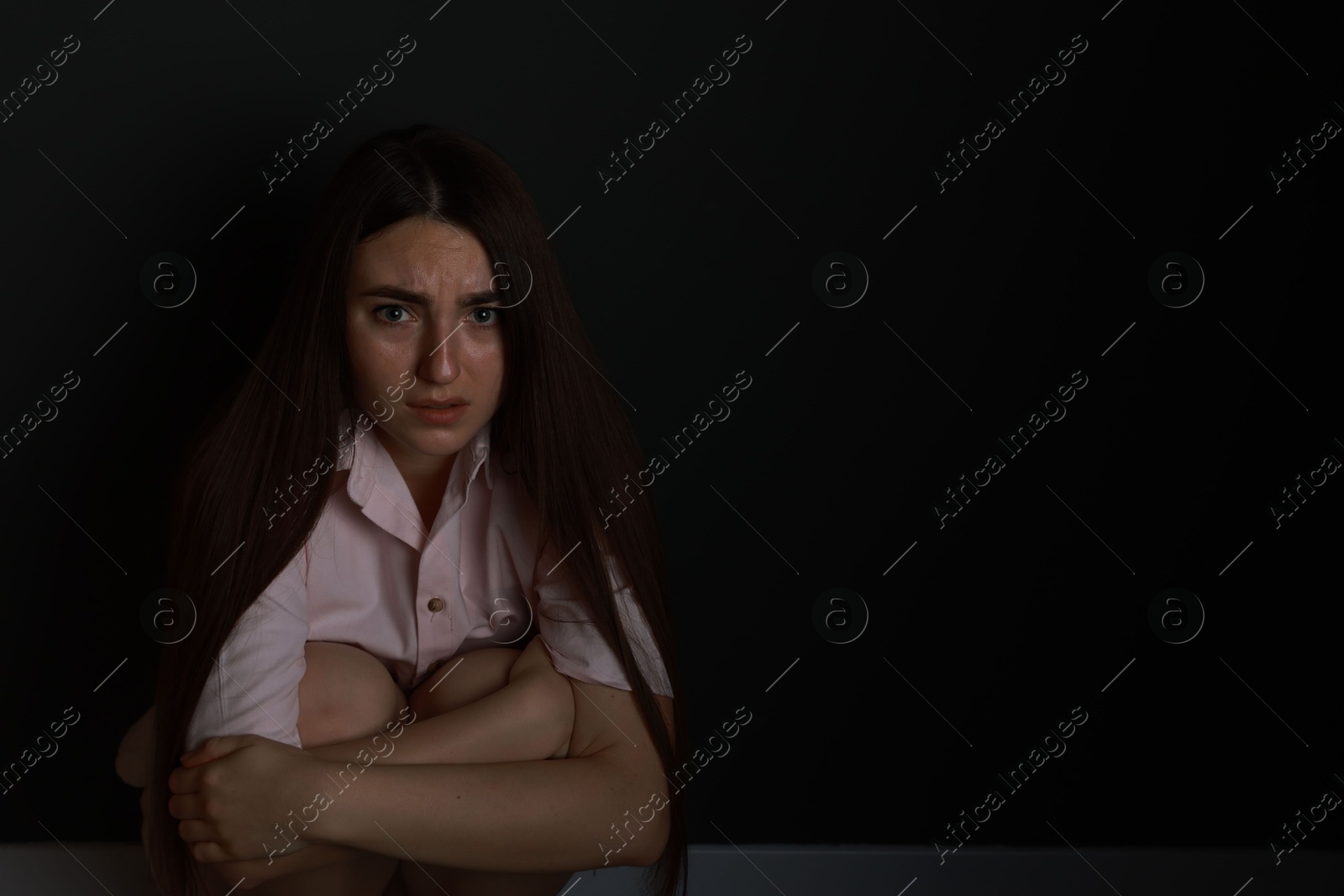 Photo of Fear of darkness. Scared young woman on black background, space for text