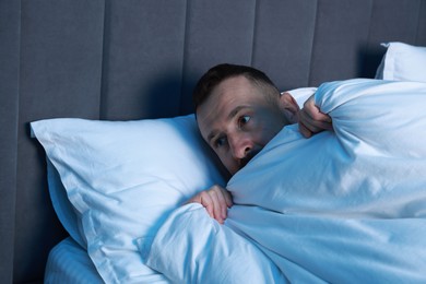 Photo of Fear of darkness. Scared man lying on bed in room at night