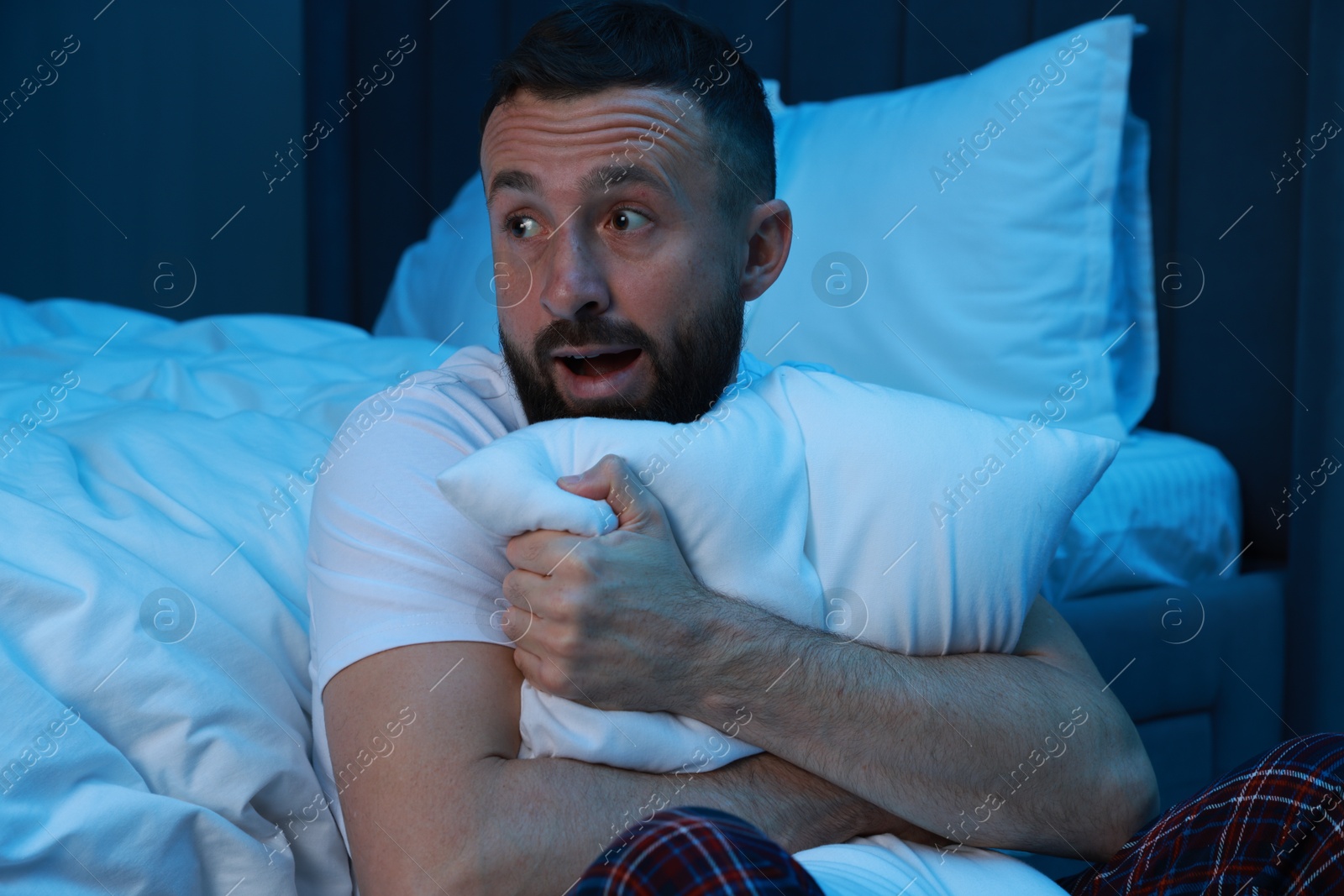 Photo of Fear of darkness. Scared man hugging pillow in bedroom at night