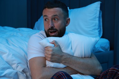 Fear of darkness. Scared man hugging pillow in bedroom at night