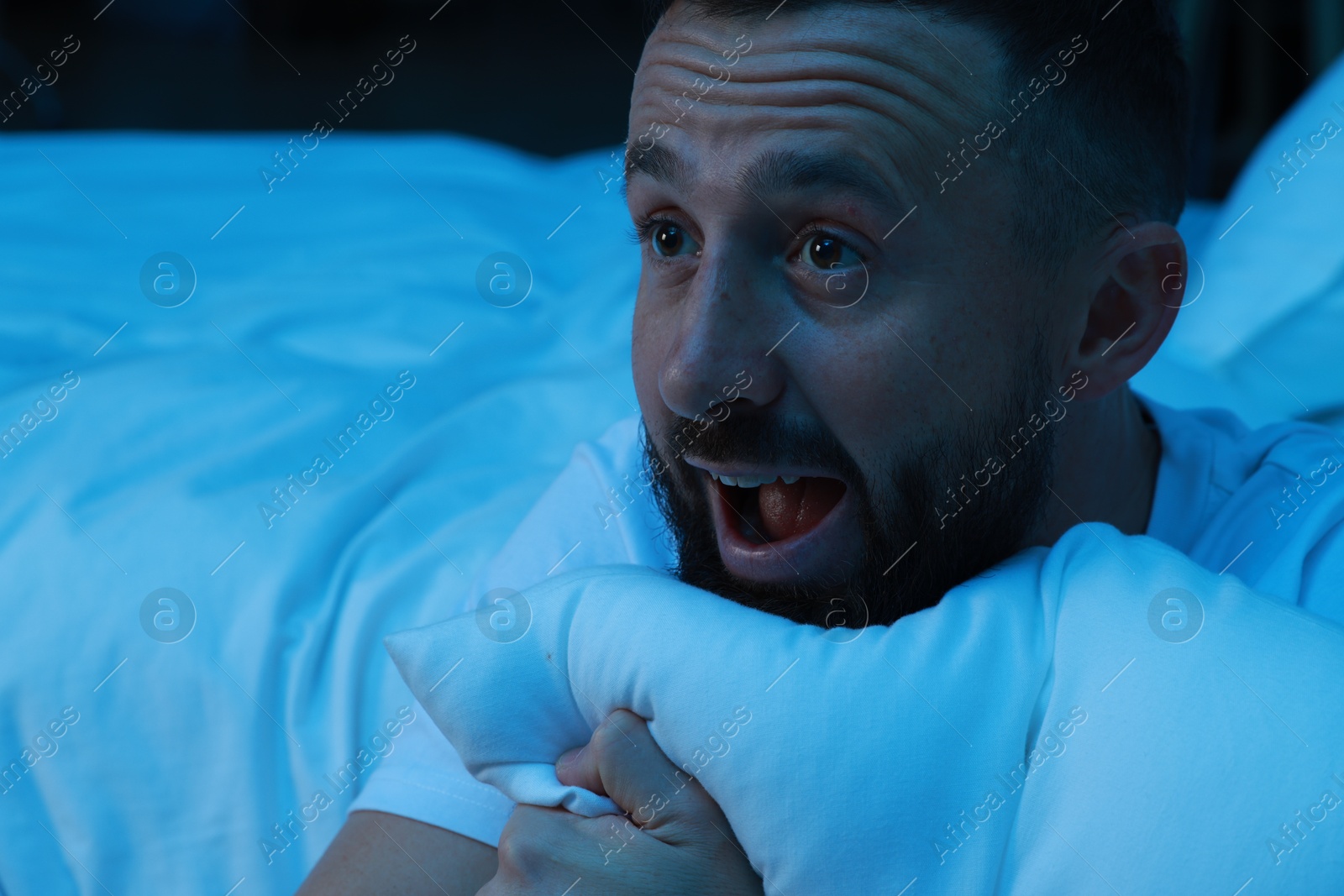 Photo of Fear of darkness. Scared man hugging pillow in bedroom at night