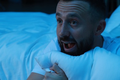 Fear of darkness. Scared man hugging pillow in bedroom at night