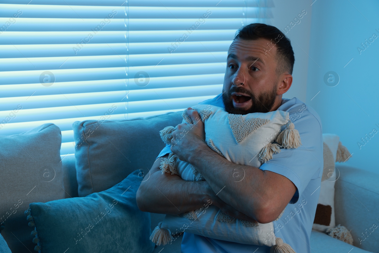 Photo of Fear of darkness. Scared man hugging pillow on couch in dark room