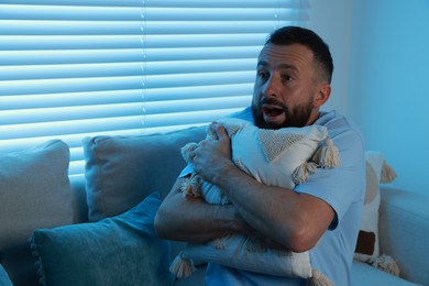 Photo of Fear of darkness. Scared man hugging pillow on couch in dark room