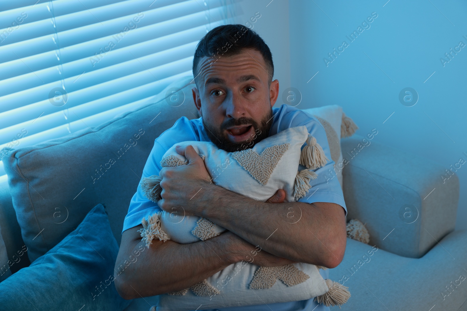 Photo of Fear of darkness. Scared man hugging pillow on couch in dark room