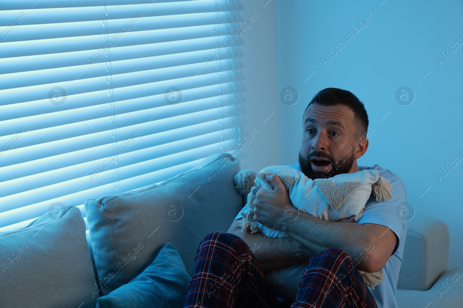 Photo of Fear of darkness. Scared man hugging pillow on couch in dark room, space for text