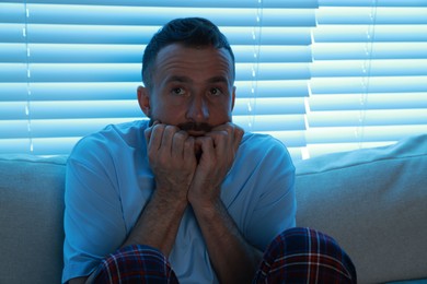 Fear of darkness. Scared man on couch in dark room