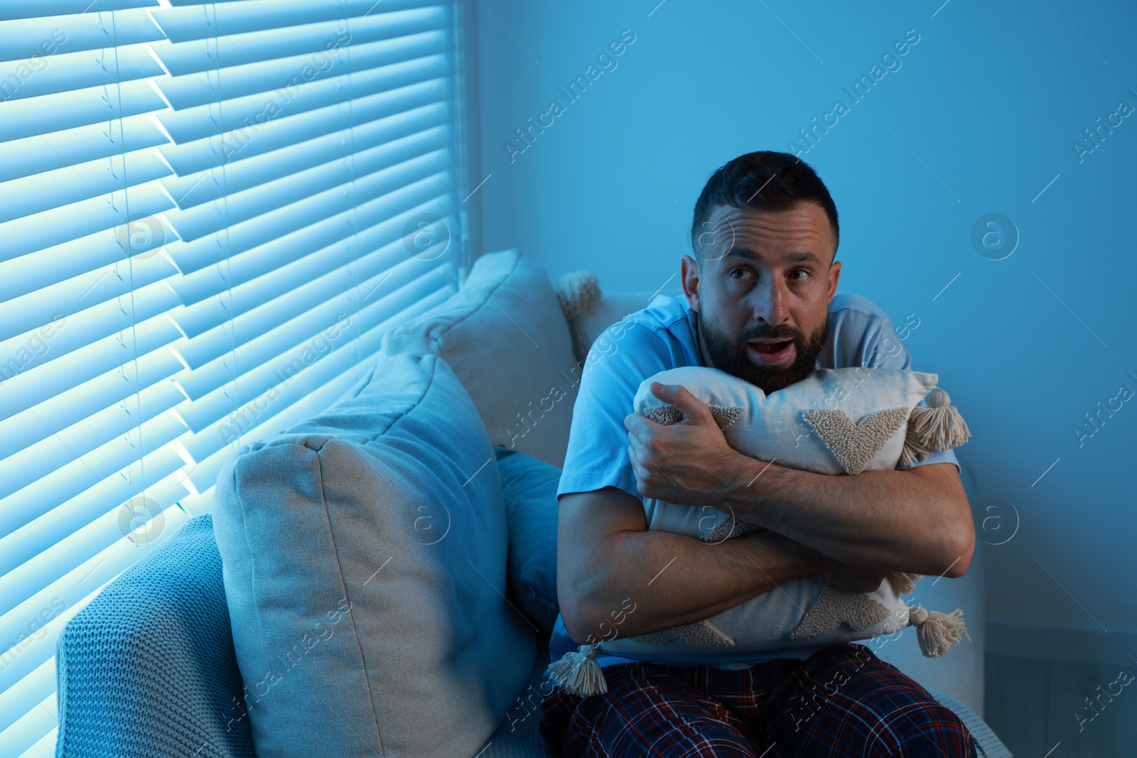 Photo of Fear of darkness. Scared man hugging pillow on couch in dark room, space for text