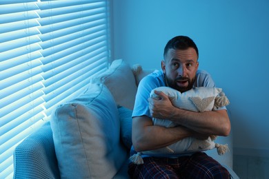 Photo of Fear of darkness. Scared man hugging pillow on couch in dark room, space for text