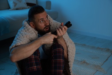 Photo of Fear of darkness. Scared man with blanket and flashlight indoors at night, space for text