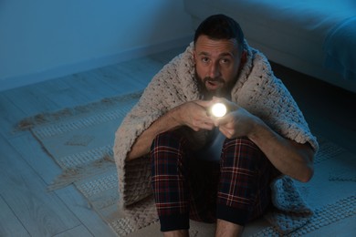 Fear of darkness. Scared man with blanket and flashlight indoors at night