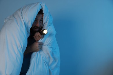 Fear of darkness. Scared man with blanket and flashlight on light grey background, space for text