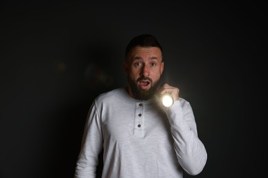 Photo of Fear of darkness. Scared man with flashlight on black background