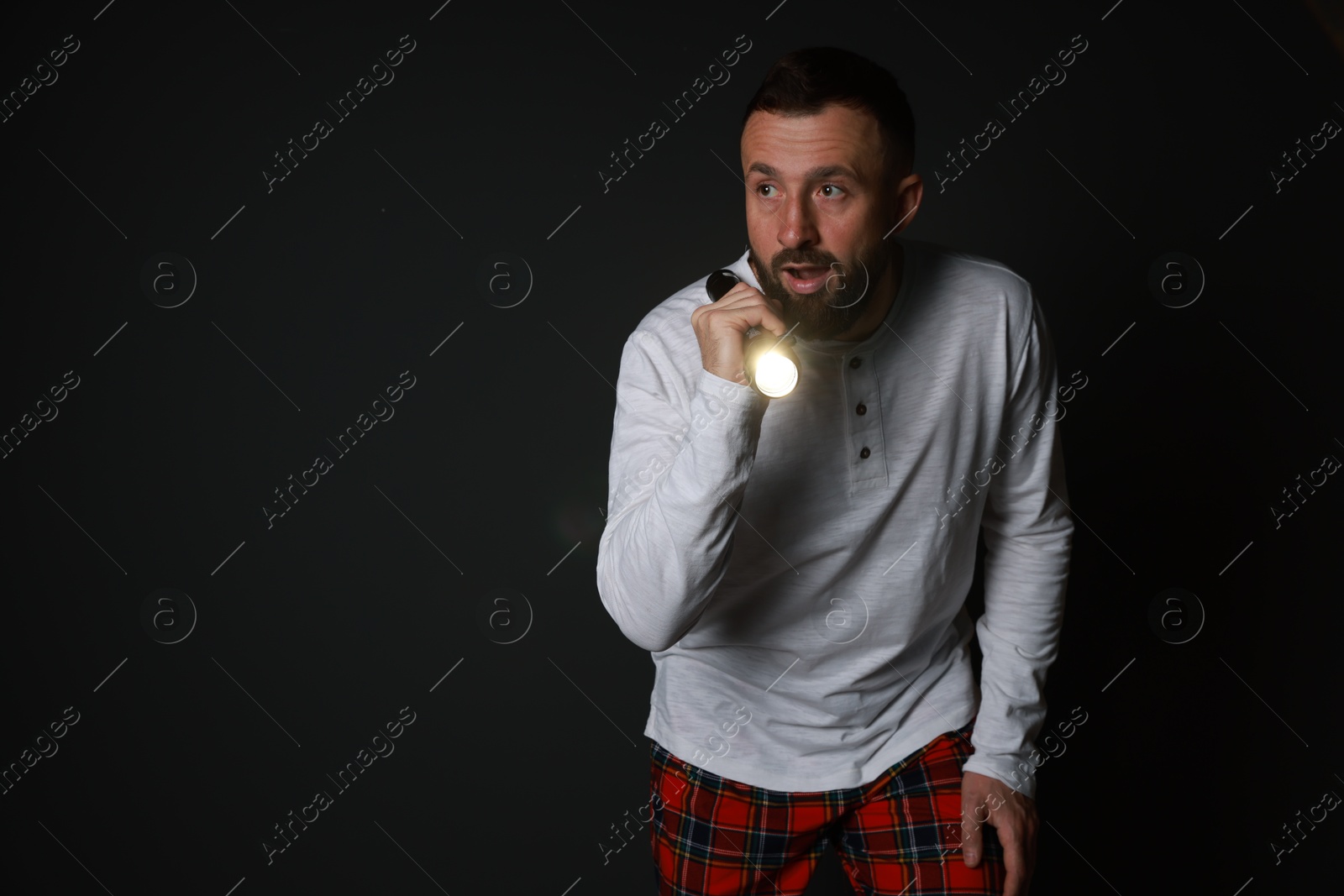 Photo of Fear of darkness. Scared man with flashlight on black background, space for text