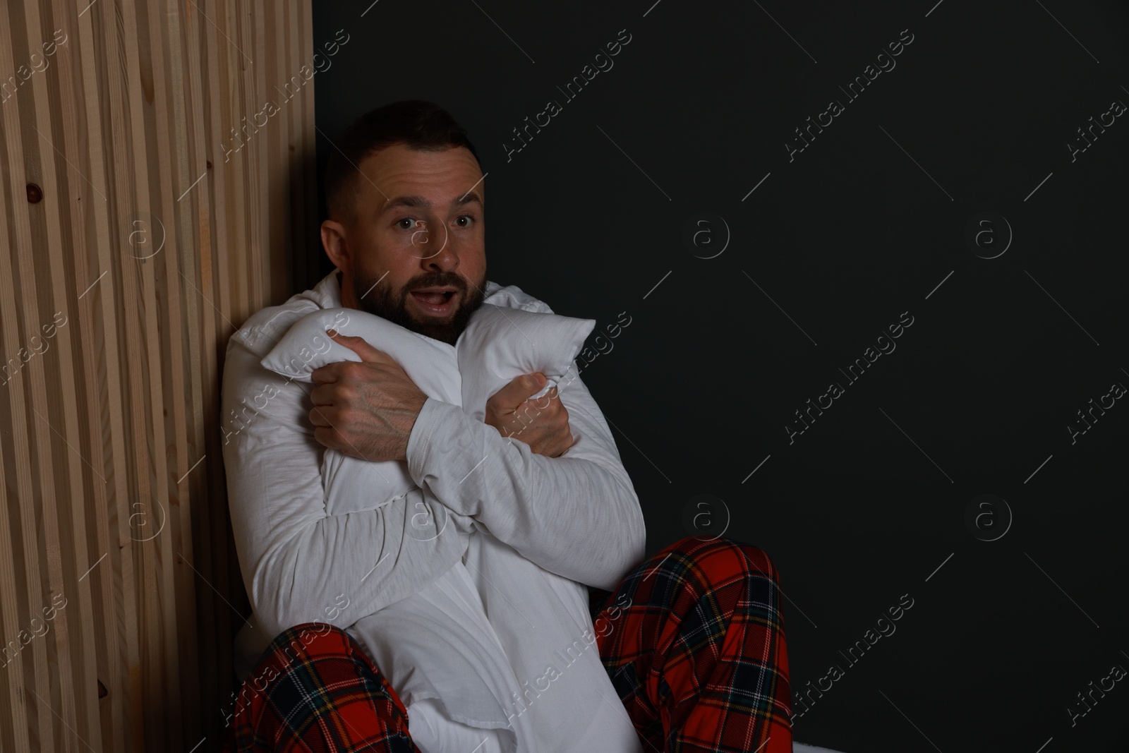 Photo of Fear of darkness. Scared man hugging pillow indoors at night