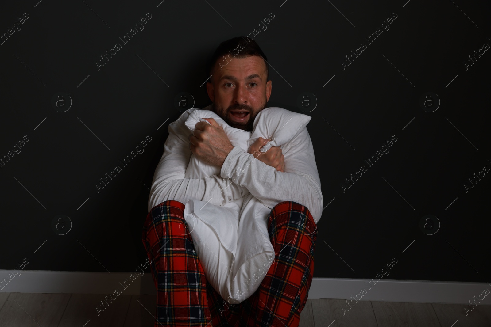 Photo of Fear of darkness. Scared man hugging pillow indoors at night