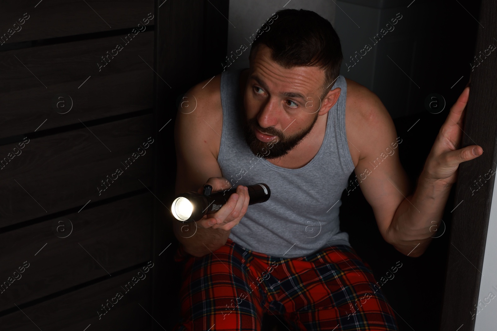 Photo of Fear of darkness. Scared man with flashlight in room at night