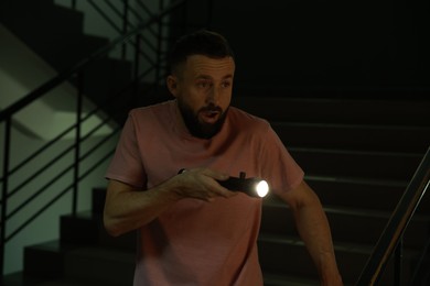 Photo of Fear of darkness. Scared man with flashlight indoors at night