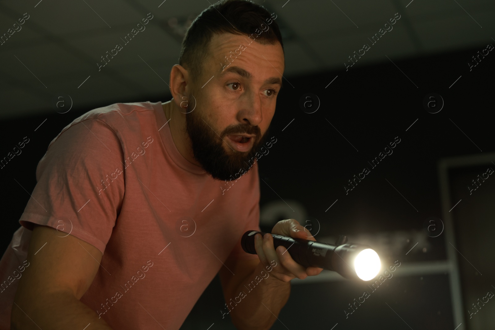 Photo of Fear of darkness. Scared man with flashlight indoors at night