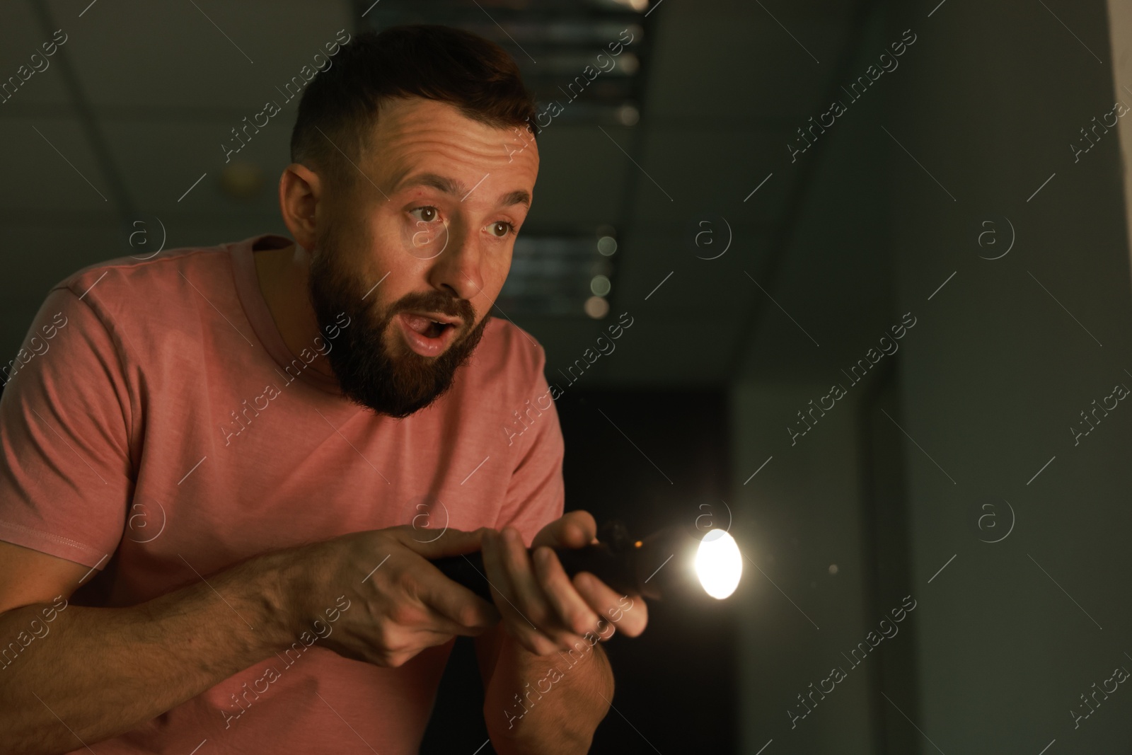 Photo of Fear of darkness. Scared man with flashlight indoors at night, space for text