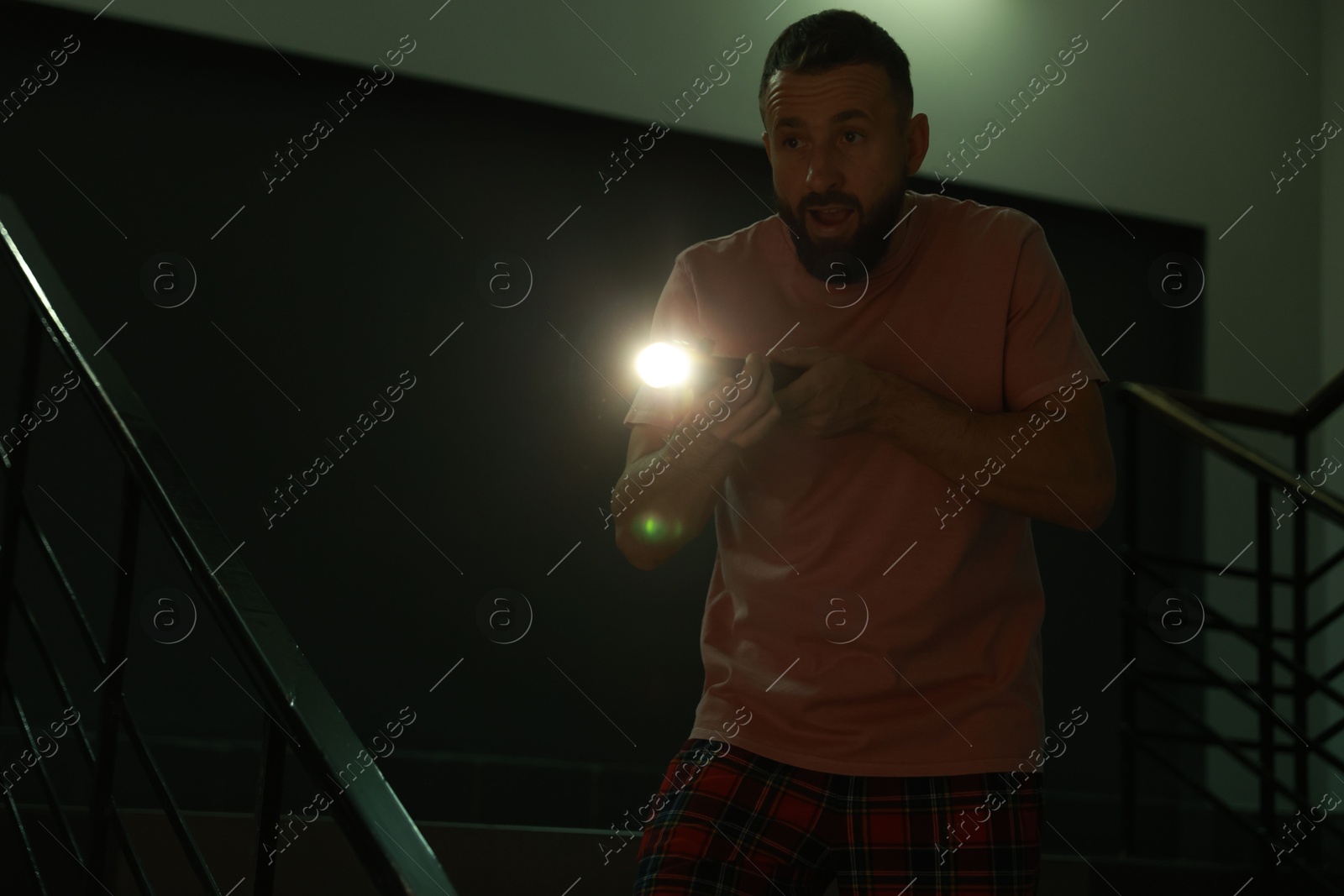 Photo of Fear of darkness. Scared man with flashlight indoors at night, space for text