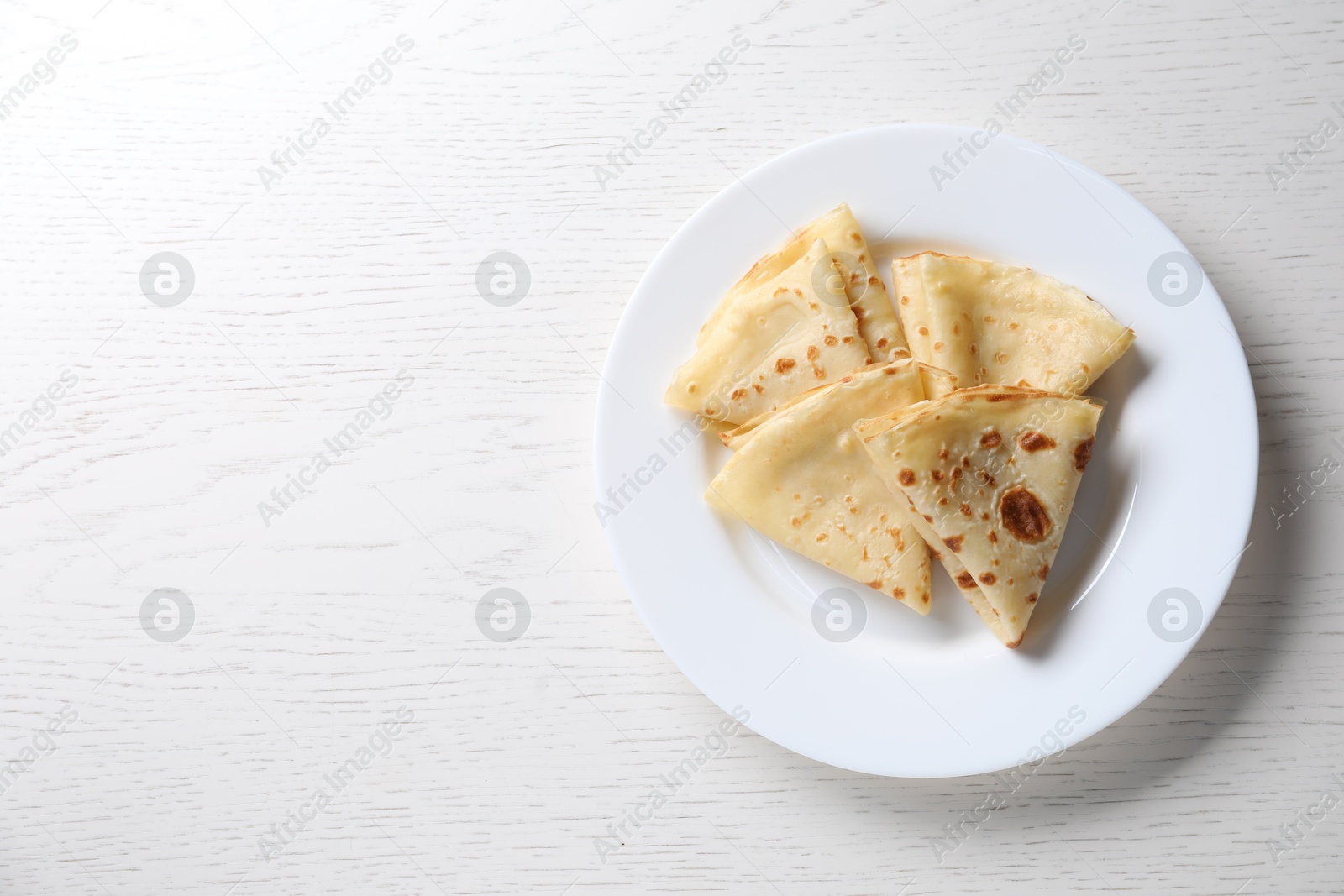 Photo of Delicious folded crepes on white wooden table, top view. Space for text