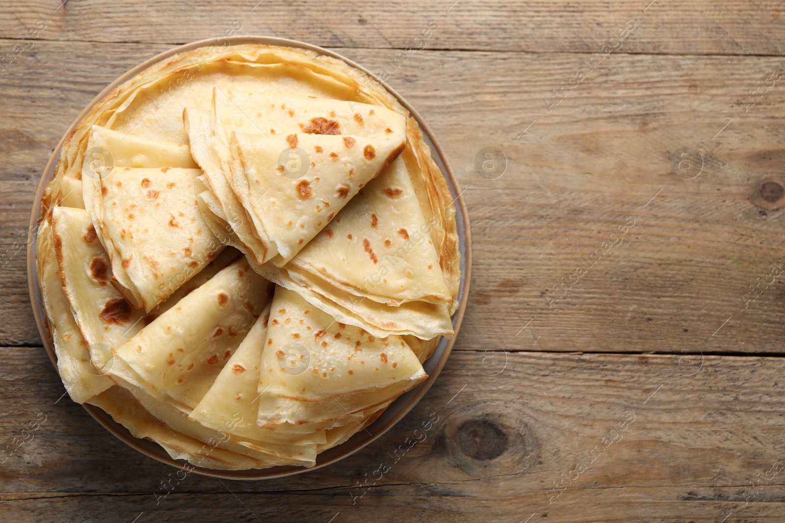 Photo of Delicious folded crepes on wooden table, top view. Space for text