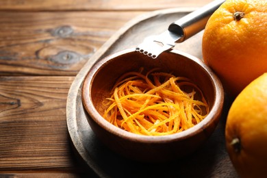 Photo of Orange zest, zester tool and fresh fruits on wooden table, closeup. Space for text