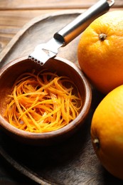 Photo of Orange zest, zester tool and fresh fruits on wooden table, closeup