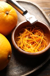 Photo of Orange zest, zester tool and fresh fruits on wooden table, closeup