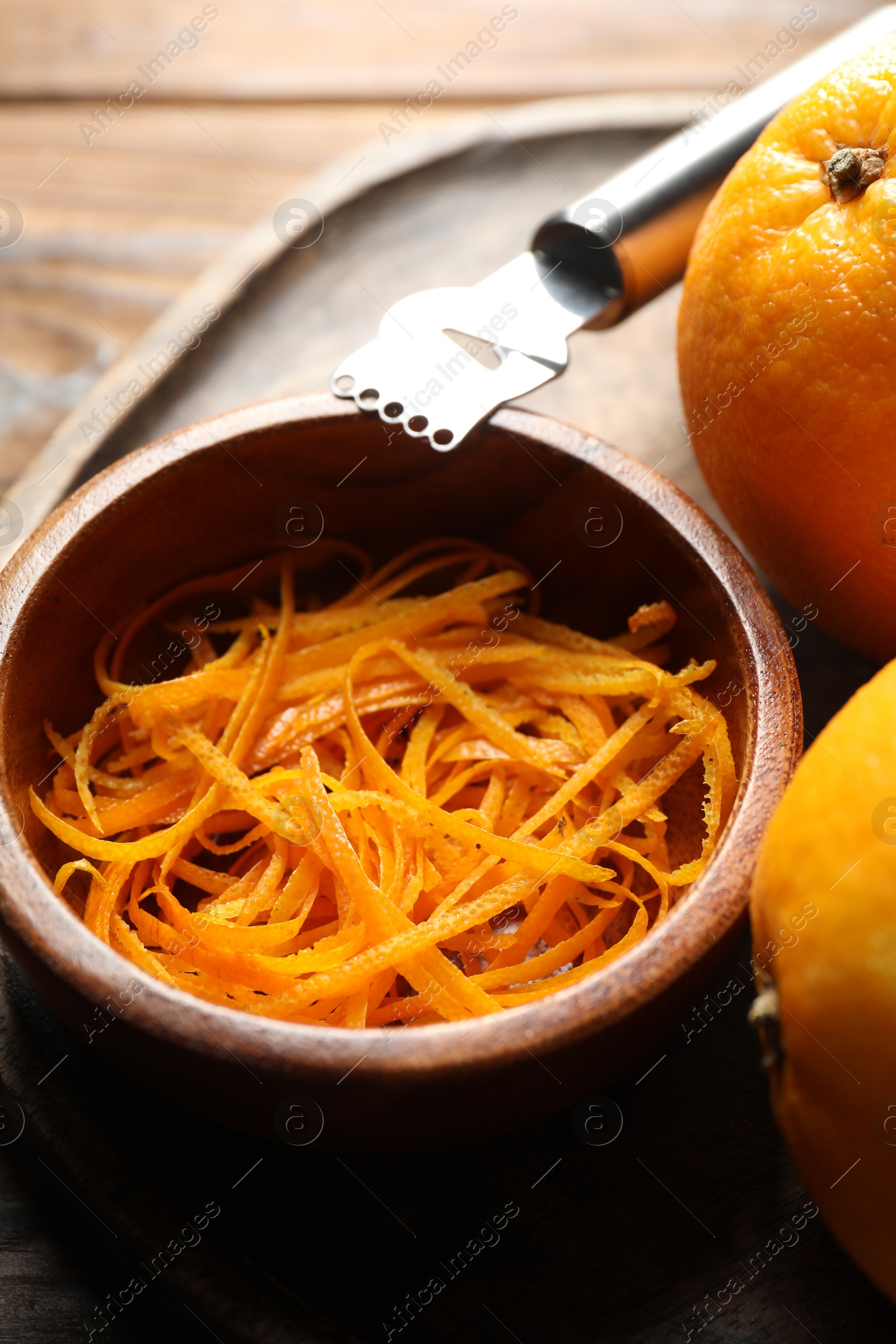 Photo of Orange zest, zester tool and fresh fruits on wooden table, closeup