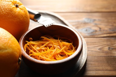 Photo of Orange zest, zester tool and fresh fruits on wooden table, closeup. Space for text