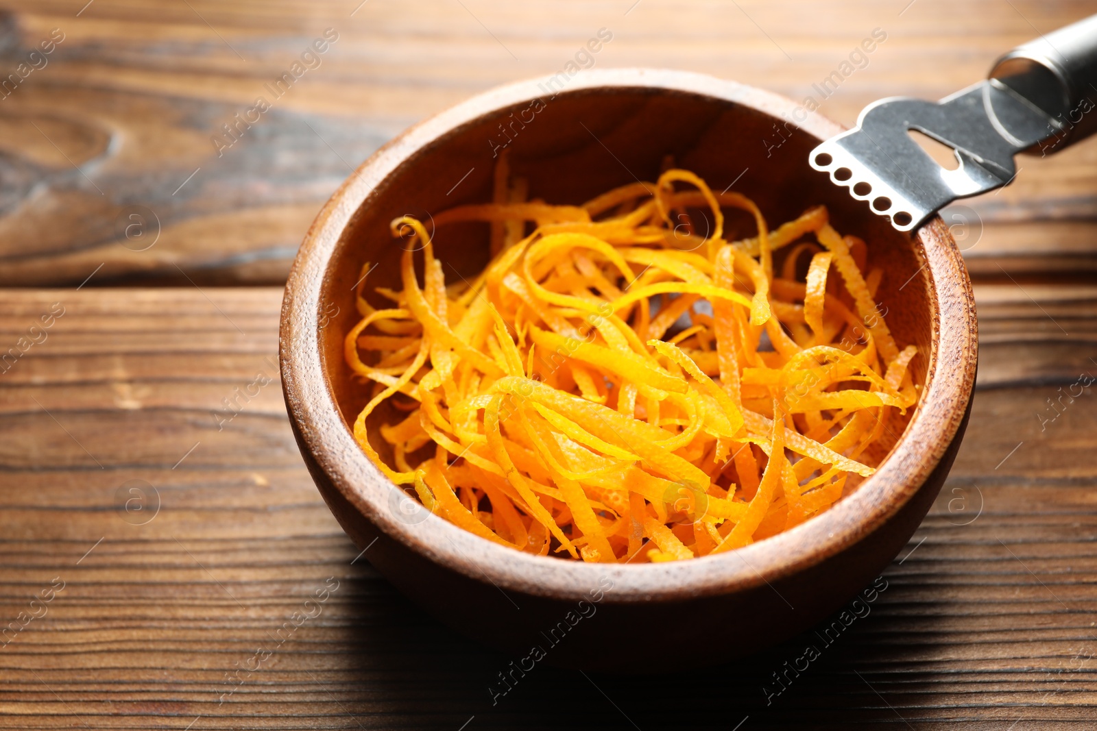 Photo of Fresh orange zest in bowl and zester tool on wooden table, closeup