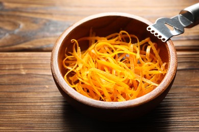 Photo of Fresh orange zest in bowl and zester tool on wooden table, closeup