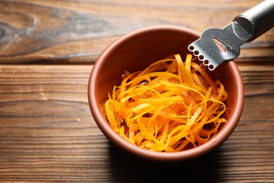 Photo of Fresh orange zest in bowl and zester tool on wooden table, closeup. Space for text