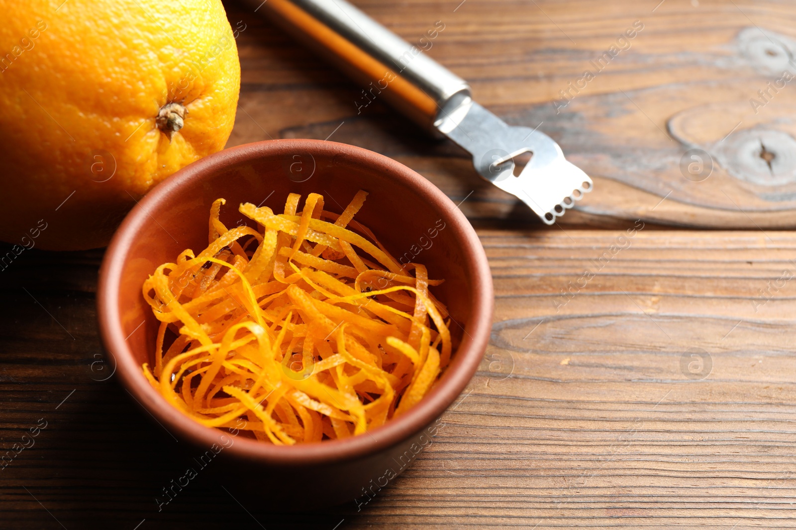 Photo of Orange zest, zester tool and fresh fruit on wooden table, closeup. Space for text