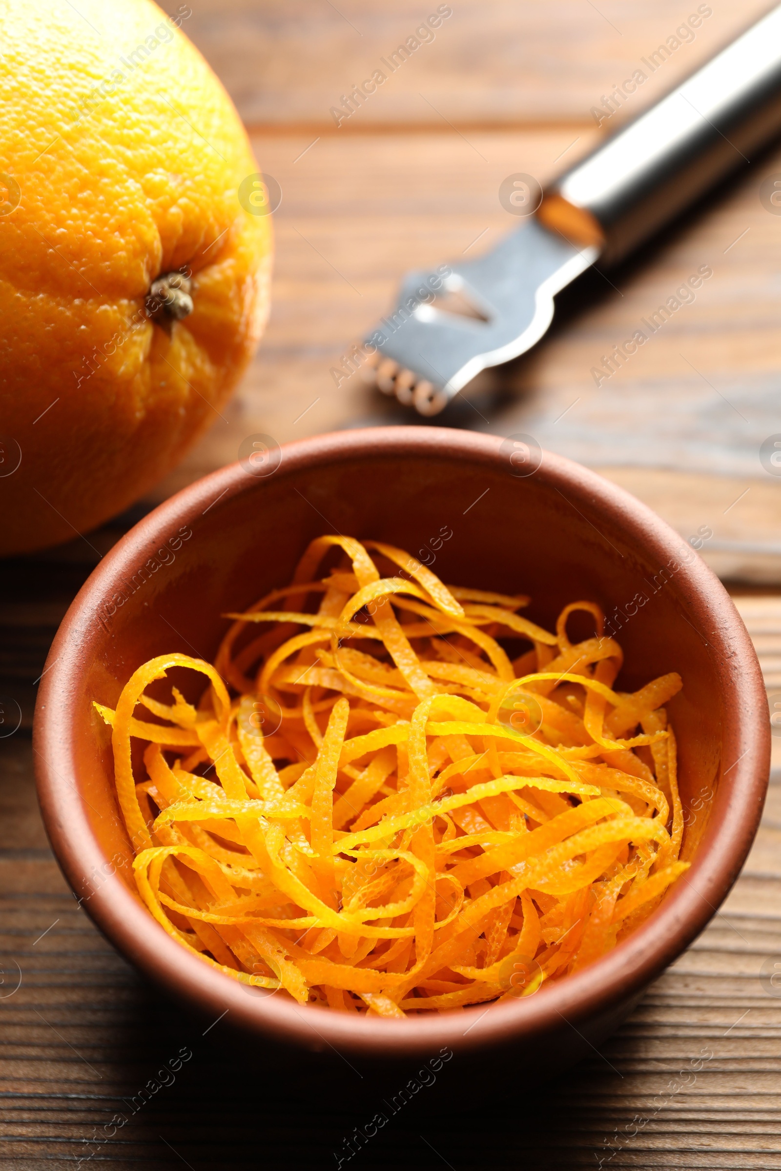 Photo of Orange zest, zester tool and fresh fruit on wooden table, closeup