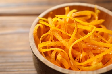 Photo of Fresh orange zest in bowl on wooden table, closeup